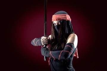 Beautiful samurai woman warrior with a sword in studio on red dark background © Vitte Yevhen