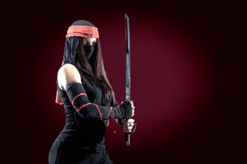 Beautiful samurai woman warrior with a sword in studio on red dark background © Vitte Yevhen