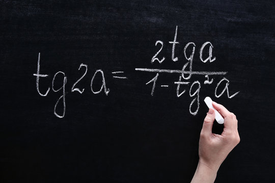 Female hand writing maths formulas on chalkboard