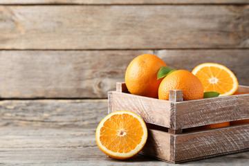 Orange fruit with green leafs in crate on grey wooden table