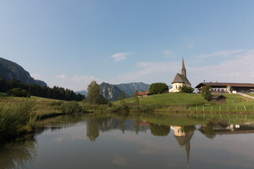 Fototapeta premium Inzell, Germany - August 5, 2018: View of the Nikolauskirche church in the Bavarian community of Inzell with the Alps in the background.