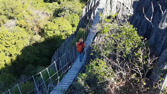 Hiker tourist walks over suspended rope bridge over gorge in Madagascar Tsingy de Bemaraha national park