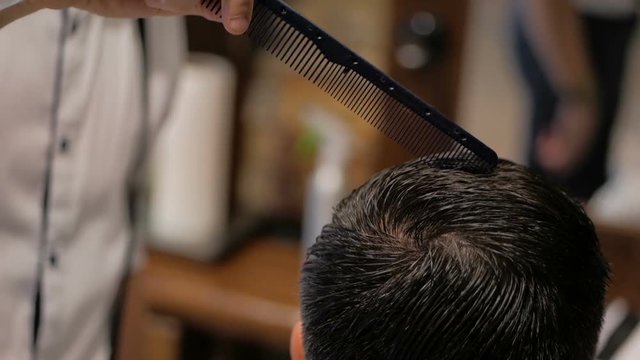 Hairdresser cuts hair to man in barbershop close-up. man's haircut