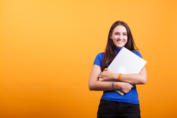 Cheerful beautiful young woman holding laptop over yellow background