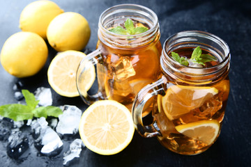 Ice tea in glass jars with lemon and mint leafs on wooden table