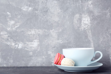 Cup of coffee with sweet macarons on grey wooden table