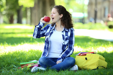 Young girl with apple and backpack sitting in the park