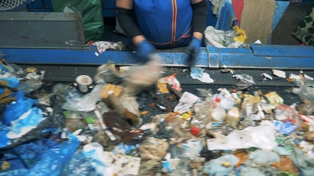 A woman sorts trash on a conveyor, close up.