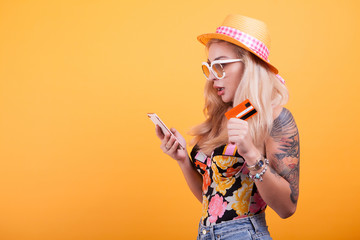 Happy attractive young woman holding and showing credit card in studio over yellow background