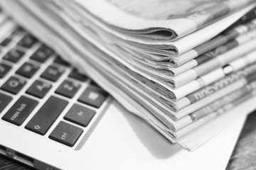 Newspapers and laptop. Pile of daily papers with news on the computer. Pages with headlines, articles folded and stacked on keypad of electronic device. Modern gadget and old journals, focus on paper 