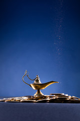 Magic lamp of wishes on stacks of gold coins with smoke coming out from the lamp. Studio shooting.