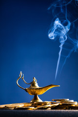 Magic lamp of wishes on stacks of gold coins with smoke coming out from the lamp. Studio shooting.