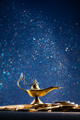 Magic lamp of wishes on stacks of gold coins with golden dust. Studio shooting.