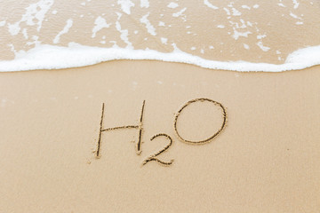 Word H2O written in sand beach, water concept.
