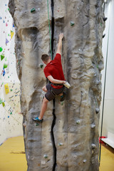 Photo from back of man climbing up boulder in gym