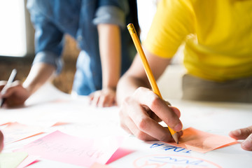 Close up of unrecognizable man writing ideas on post-it notes while planning project in office