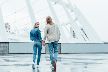 rear view of young couple holding hands and walking by parking on cloudy day