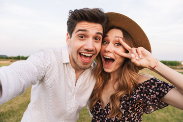Cute loving couple outdoors hugging with each other take a selfie by camera with peace gesture.