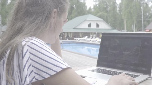 The girl is working in the fresh air by the pool. Working on a laptop. S-log, ungraded