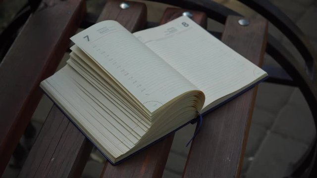 Wind turns the pages of open Notebook lies bench in park, business concept