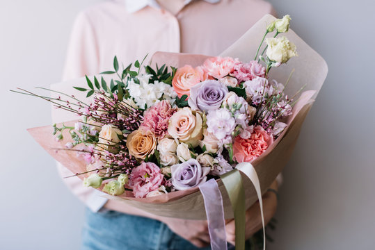 Fototapeta Very nice florist woman holding a big beautiful fresh flower bouquet of roses, carnations, eustoma, pistachios in pink and lavender colors on the grey wall background, close up view