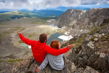 Naklejka premium Atmospheric moment for lovers in the mountains. Hiking woman and man standing on the top of the mounting and looking at a beautiful landscape. Travel Lifestyle and survival concept rear view