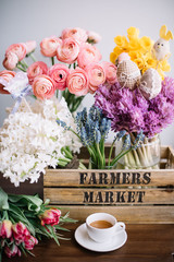 Beautiful spring flowers on the wooden table with easter decoration festive set: fresh blossoming ranunculus, Narcissus, hyacinths and tulips in the wooden box with espresso and cute toy chicken