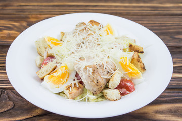 Caesar salad with chicken, in a plate on a wooden background