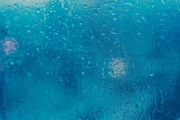 Blue texture of drops on the glass, blurred city lights in the evening city.