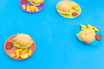 Sandwiches, hamburgers and French fries are served on a blue table for children.