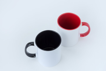 Two white mugs, with a red and black handle on a white background.  Isolated.  View from above.