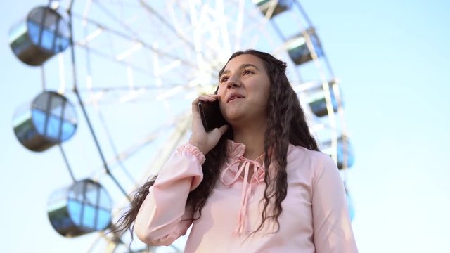 The girl is talking on the phone standing near the Ferris wheel .4K.