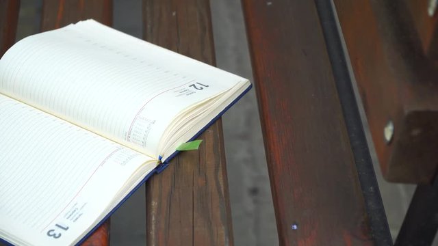 Wind turns the pages of open Notebook lies bench in park, business concept