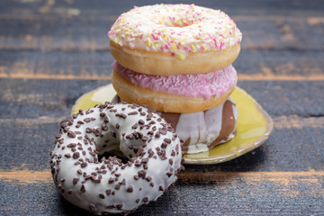 Colorful sweet glazed donuts from bakery on black wooden background close up