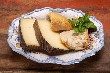 Two pieces of Manchego, queso manchego, cheese made in La Mancha region of Spain from the milk of sheep of the manchega breed served on traditional spanish board with bread