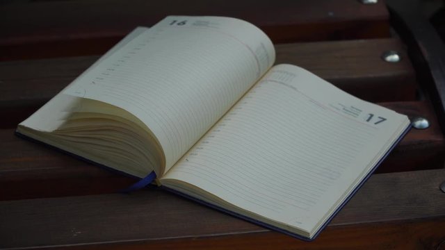Wind turns the pages of open Notebook lies bench in park, business concept