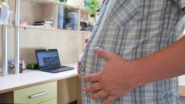 Caucasian young man's touch and check fatty abdomen at office. Obesity in the present society