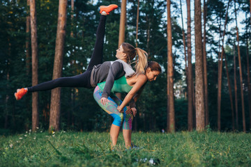 Two young sportswomen doing partner workout together in forest