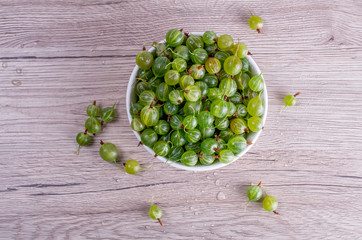 Ripe berries of a gooseberry n white plate on a wooden background with space for insert text..Flat lay, top view, copy space