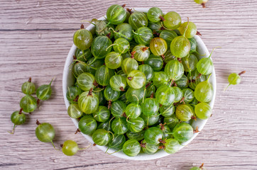 Ripe berries of a gooseberry n white plate on a wooden background. Flat lay, top view