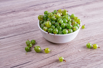 Ripe berries of a gooseberry n white plate on a wooden background with space for insert text. Top view, copy space