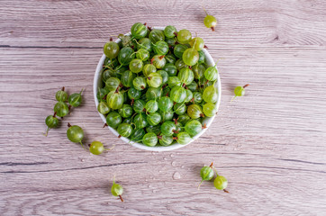 Ripe berries of a gooseberry in white plate on a wooden background with space for insert text. Flat lay, top view, copy space