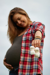blurred silhouette of a pregnant woman on a light background holding baby booties-socks