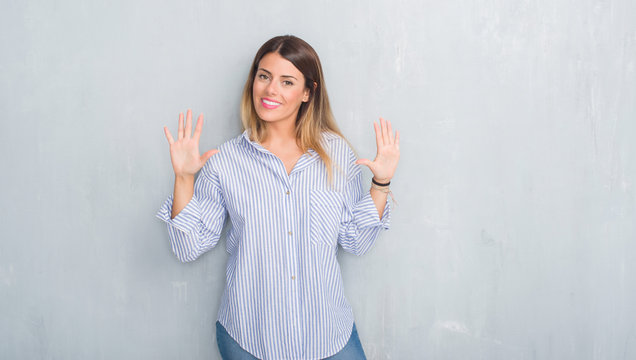 Young adult woman over grey grunge wall wearing fashion business outfit showing and pointing up with fingers number ten while smiling confident and happy.