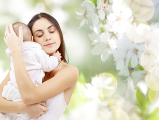 Obraz na płótnie Canvas family and motherhood concept - happy young mother holding little baby over cherry blossom background