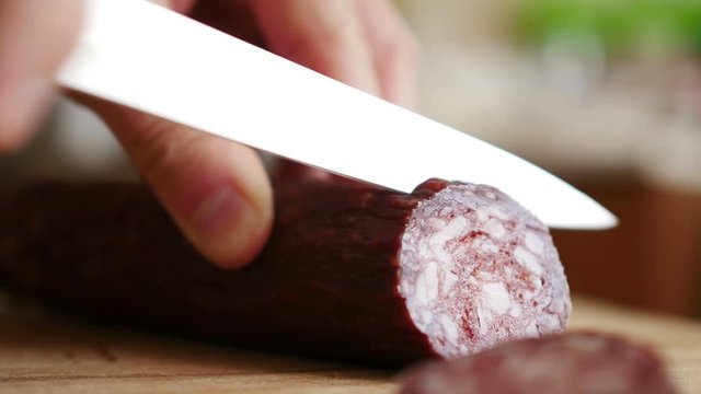 Man cuts into thin slices fatty sausage. Shooting closeup. Chef cutting salami with a knife on a wood board close up.