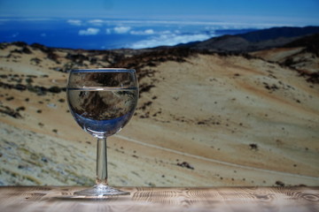A glass glass glass with clean water stands on a wooden table against a mountain landscape.