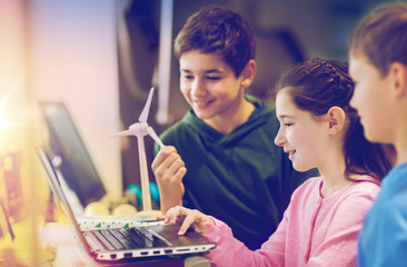 renewable energy, children, technology, science and people concept - group of happy kids or friends with laptop computer and wind turbine model at school