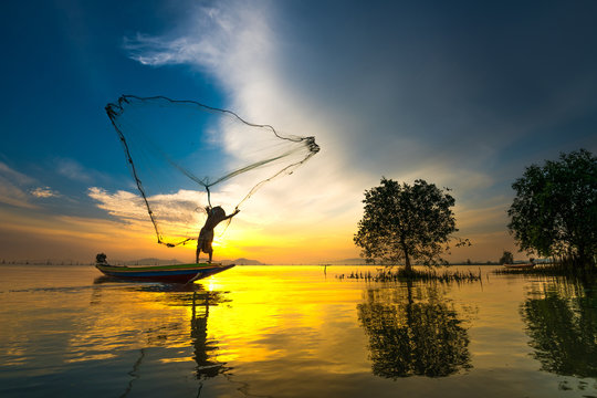 Silhouette fisherman on boat over the lake with sunrise and dramatic sky