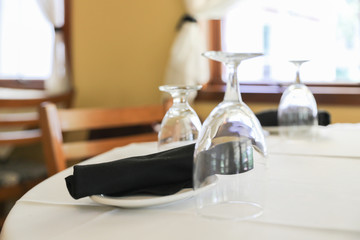 Glasses, fork, knife served for dinner in restaurant with cozy interior